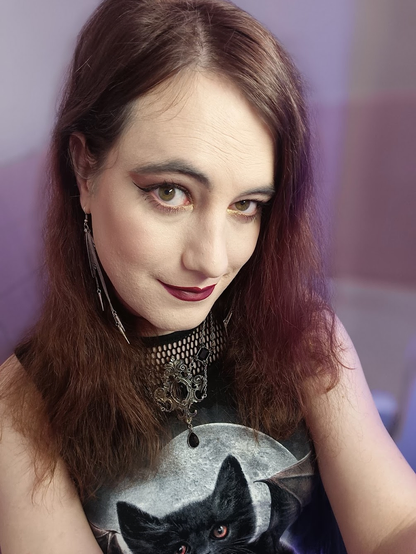 Portrait, actually (dark) red hair, a fishnet undertop, complex goth silver necklace, loong gothic earrings, corner smile, vampire cat print top.